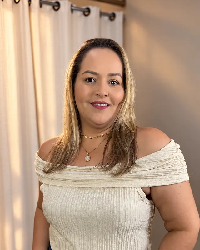 Mulher loira sorrindo, de blusa ombro a ombro off-white e jeans, no provador da Realce