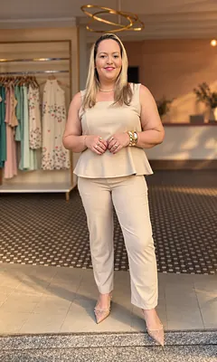 Mulher loira com conjunto bege de blusa peplum e calça reta, na porta da Realce